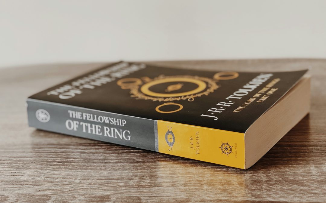 A copy of The Fellowship of the Ring by J.R.R. Tolkien lying on a wooden surface, showing the book's spine and yellow bottom edge with publisher logo